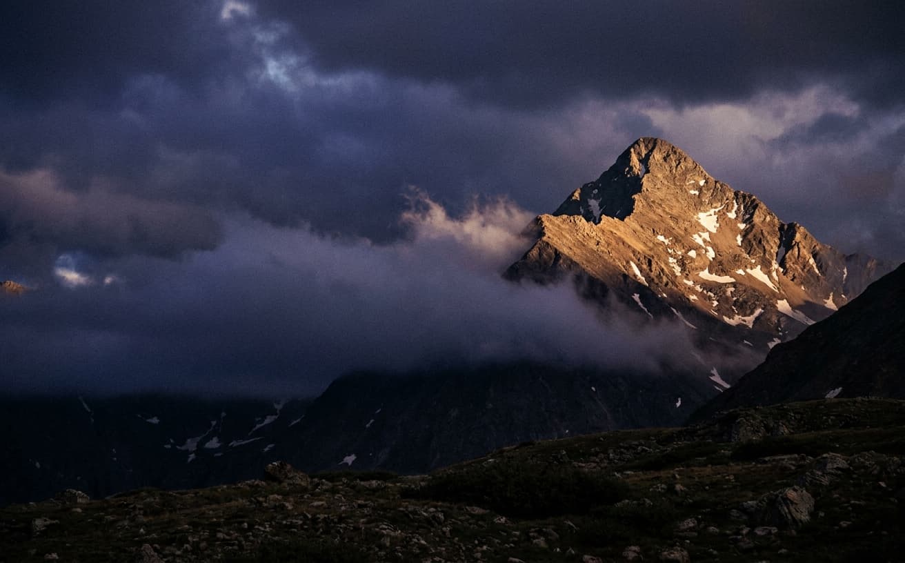 Capitol Peak summit at sunset with a shaft of golden light through cloud cover