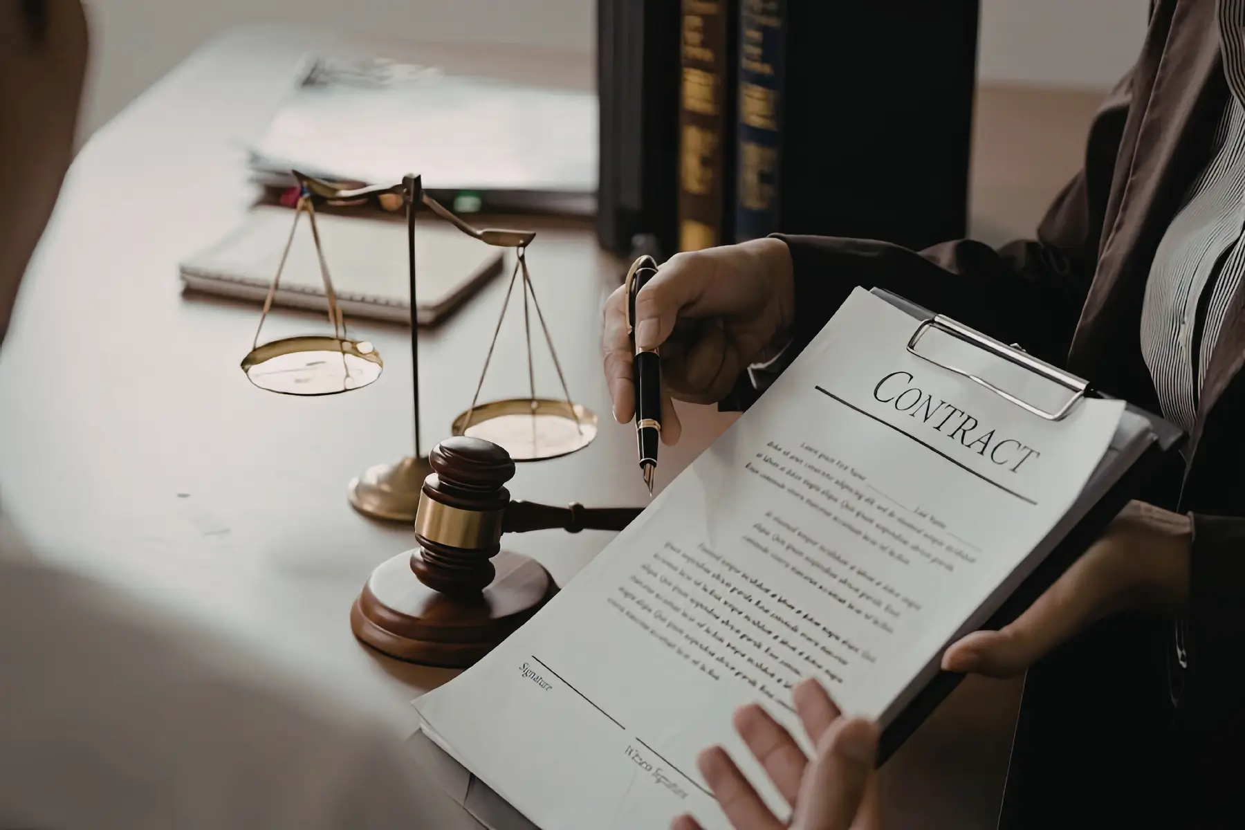 Woman in a suit holding a business contract and pointing to it with a pen with a set of legal scales, law books, and a hammer and gavel in the background